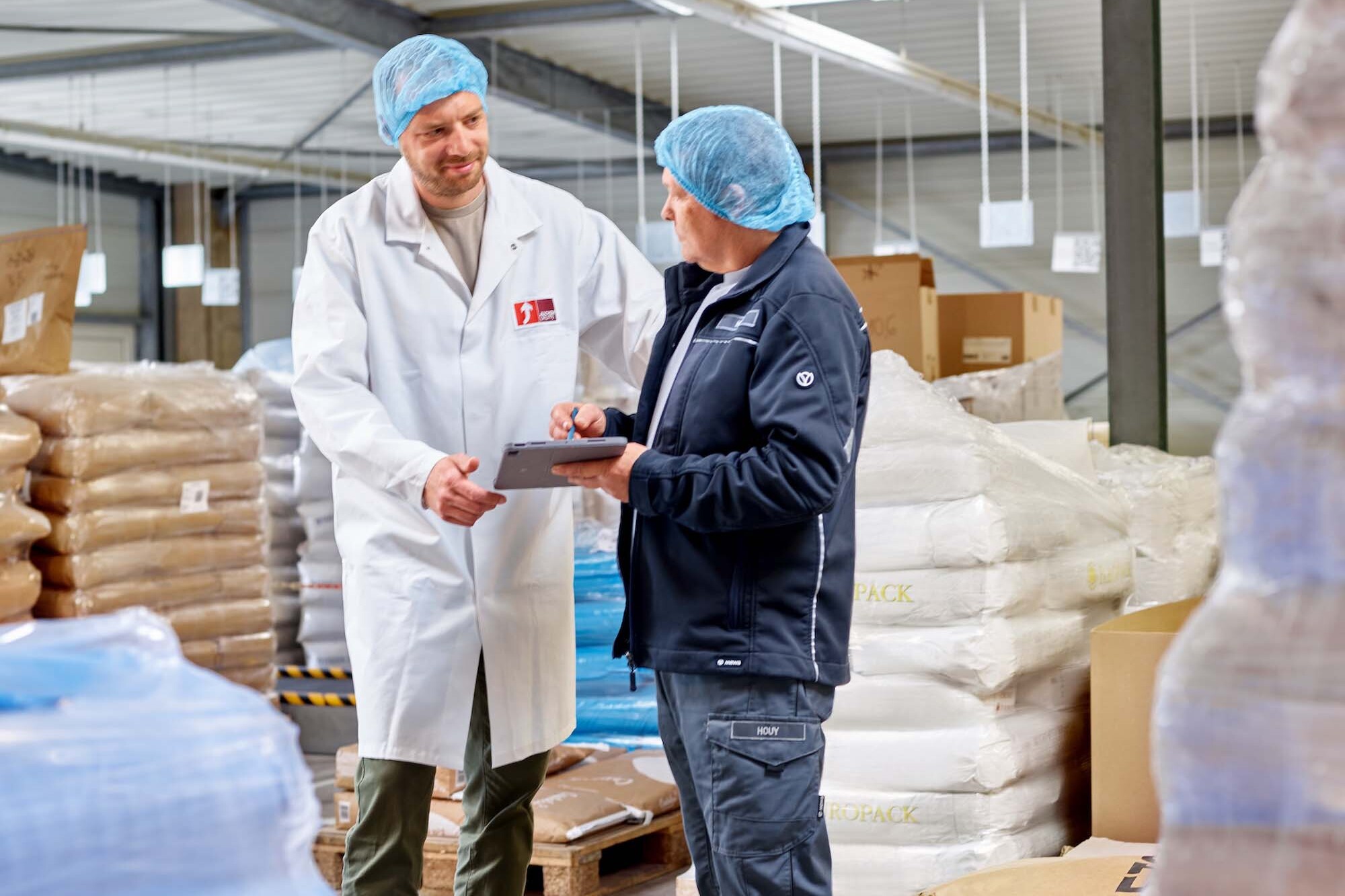 Mitarbeiter der JUCHEM GROUP prüfen Rohstoffe und Produktionsdaten digital im Lager- und Produktionsbereich.