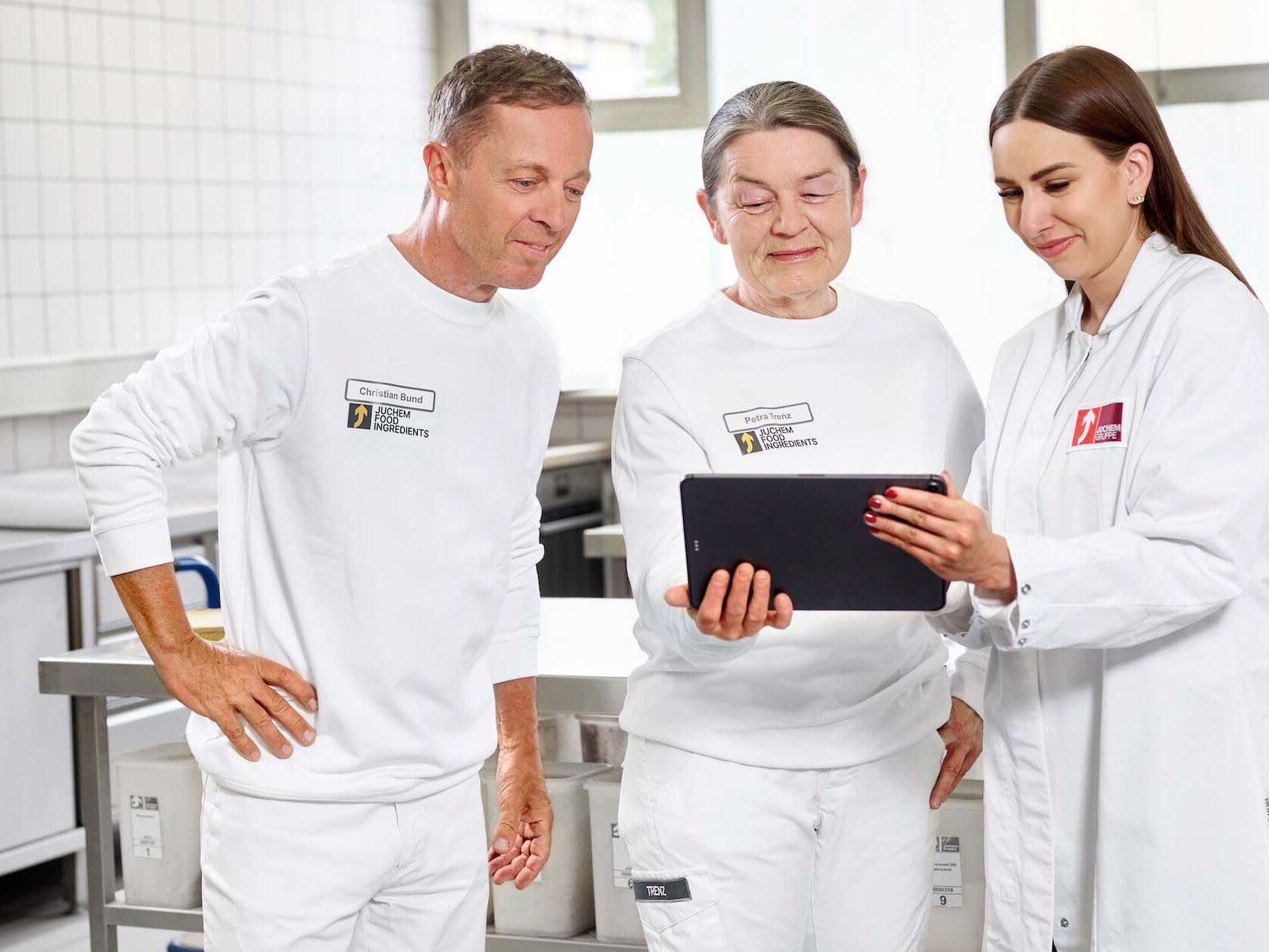 Drei Mitarbeiter der JUCHEM GROUP besprechen Produktions- und Entwicklungsprozesse gemeinsam an einem Tablet im Laborbereich.