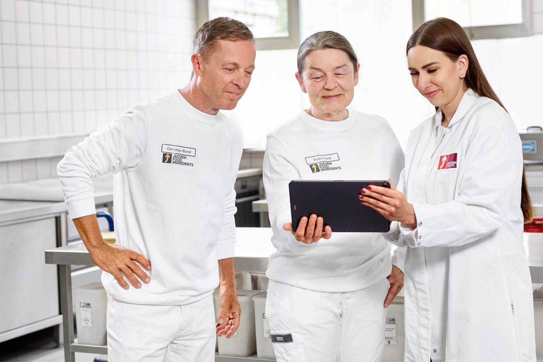 Drei Mitarbeiter der JUCHEM GROUP besprechen Produktions- und Entwicklungsprozesse gemeinsam an einem Tablet im Laborbereich.