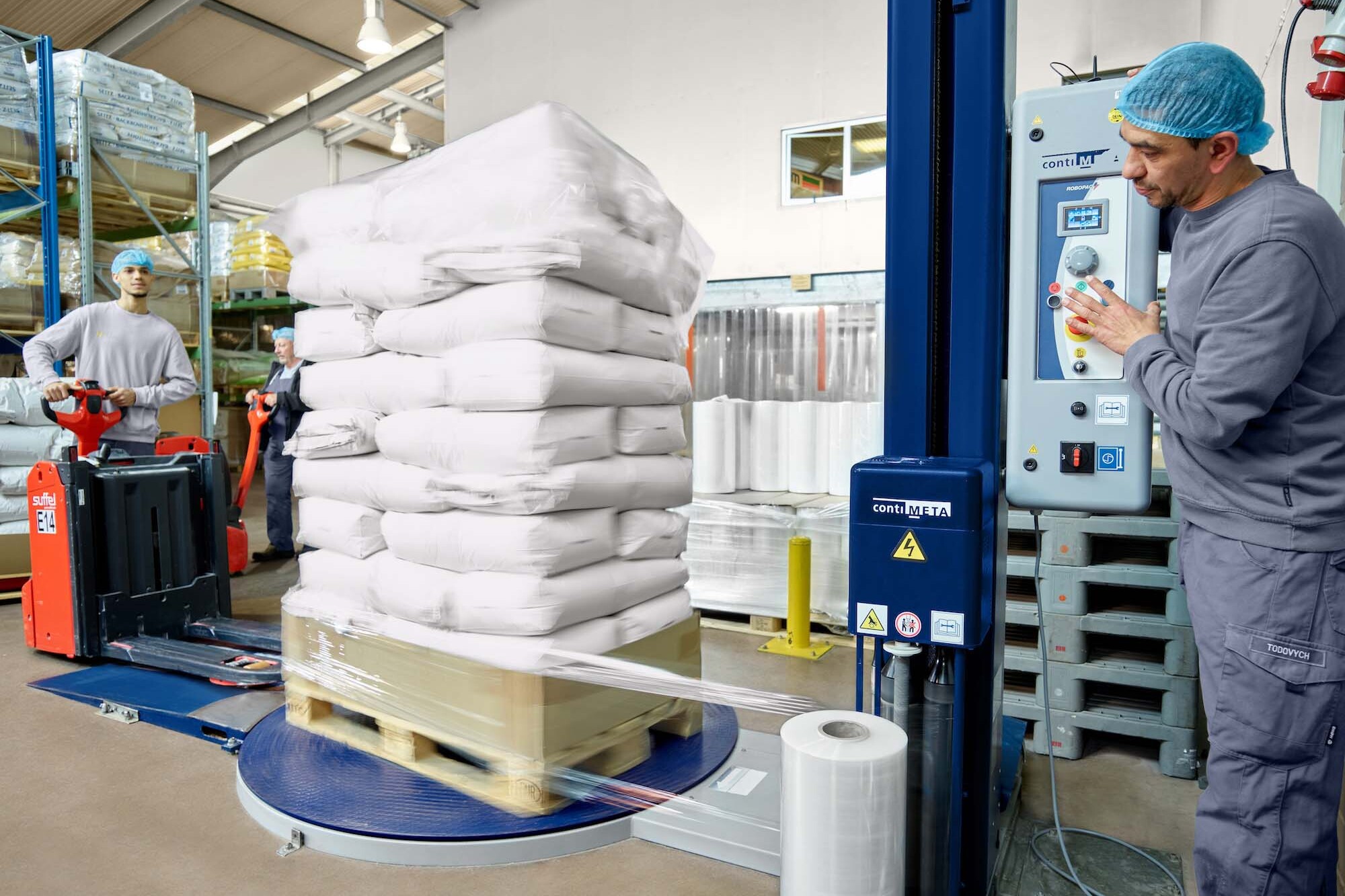 Mitarbeiter der JUCHEM GROUP sichern und verpacken Rohstoffsäcke auf Paletten im Produktions- und Lagerbereich.